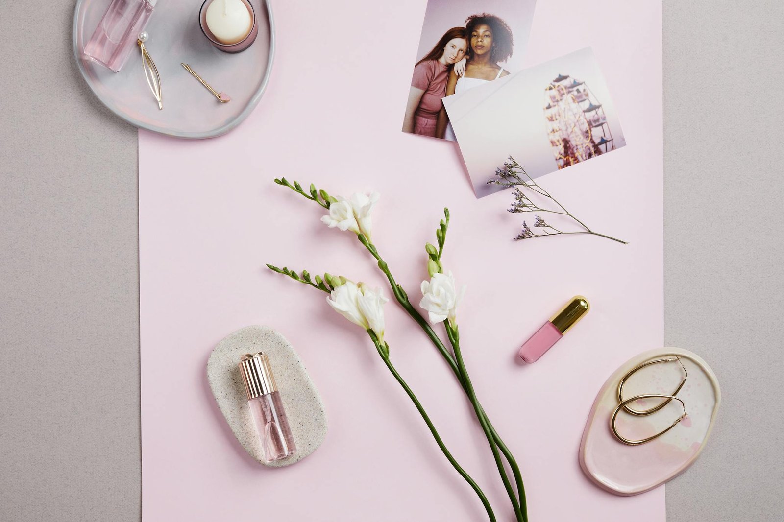 Stylish flat lay of perfume, earrings, and flowers on a pink background. Perfect for fashion and lifestyle themes.